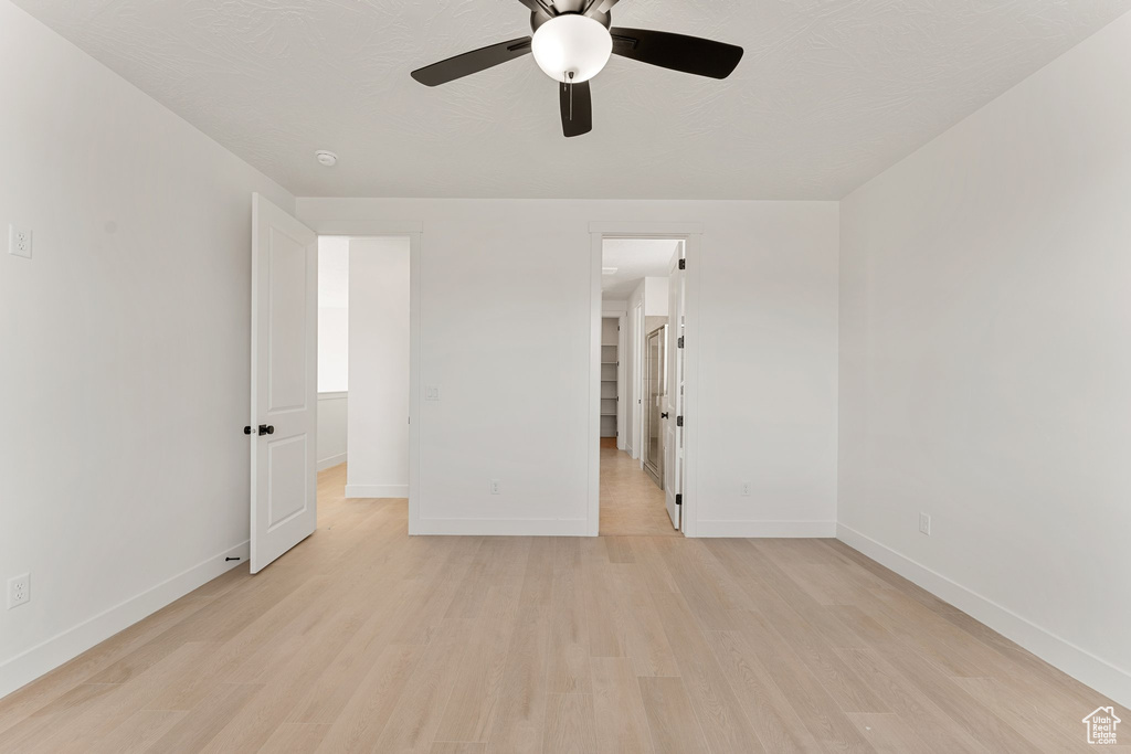 Unfurnished bedroom featuring light wood-style floors, baseboards, a walk in closet, and ceiling fan
