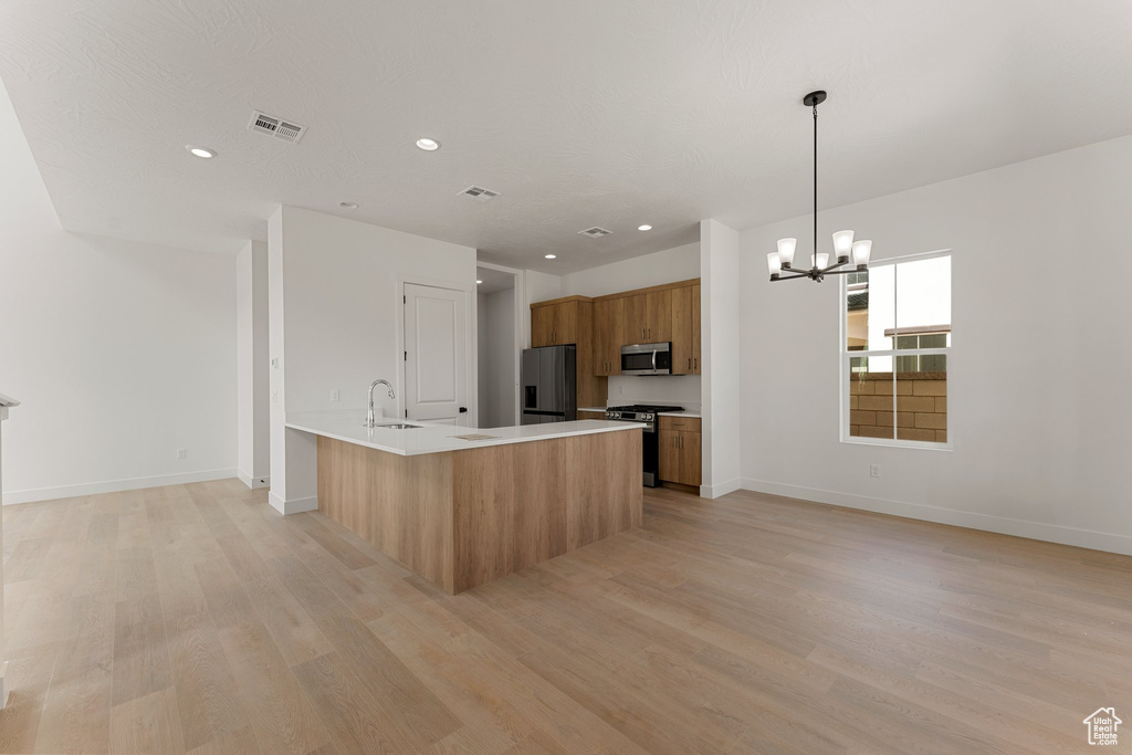 Kitchen featuring appliances with stainless steel finishes, brown cabinetry, light wood-style floors, a chandelier, and light countertops