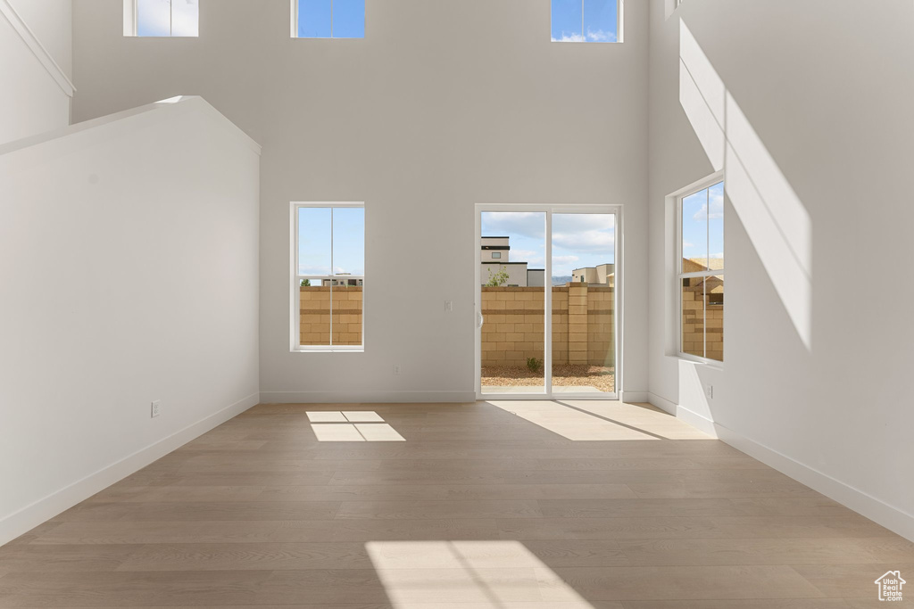 Unfurnished living room with a high ceiling, light wood-style flooring, and baseboards