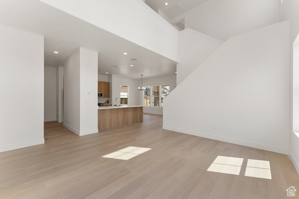 Unfurnished living room with baseboards, light wood-type flooring, recessed lighting, a sink, and a chandelier