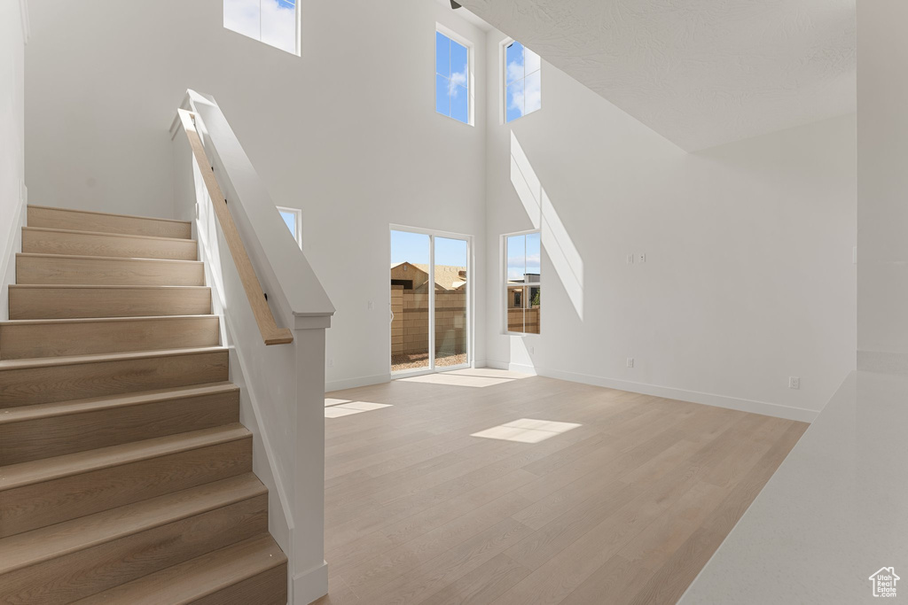 Unfurnished living room with plenty of natural light, wood finished floors, stairs, a towering ceiling, and baseboards