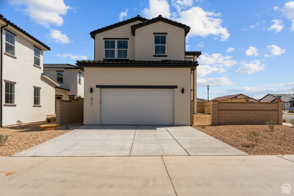 View of front of property with a tile roof, stucco siding, a garage, driveway, and fence