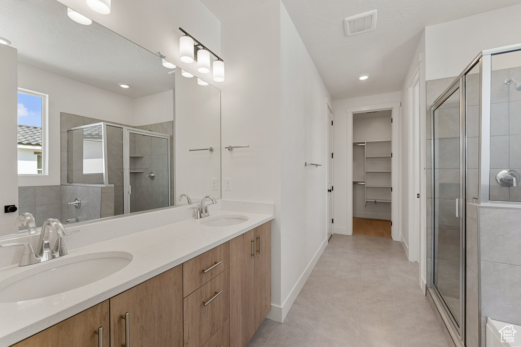 Full bathroom featuring a stall shower, a spacious closet, double vanity, baseboards, and recessed lighting