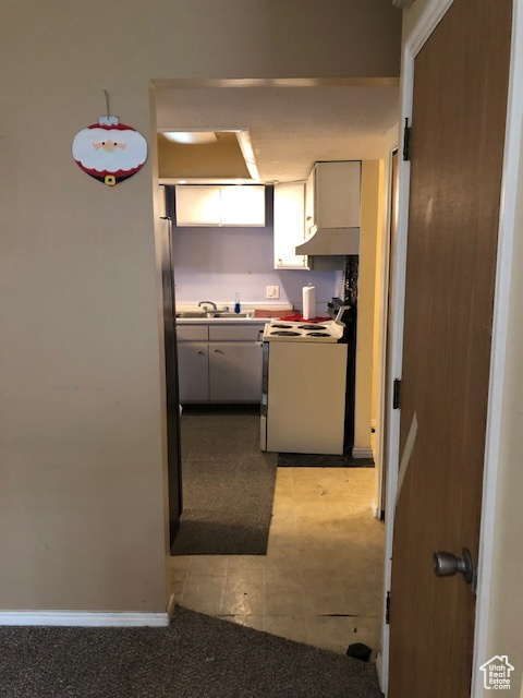 Kitchen with electric range, a sink, white cabinetry, baseboards, and light tile patterned floors