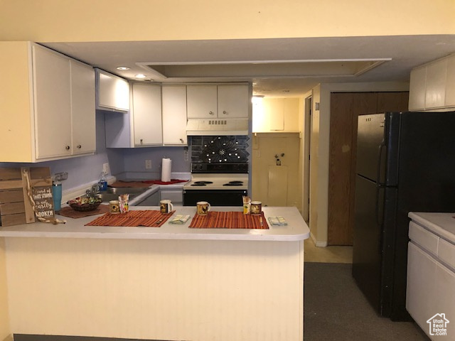 Kitchen with range with electric stovetop, a peninsula, freestanding refrigerator, white cabinetry, and under cabinet range hood