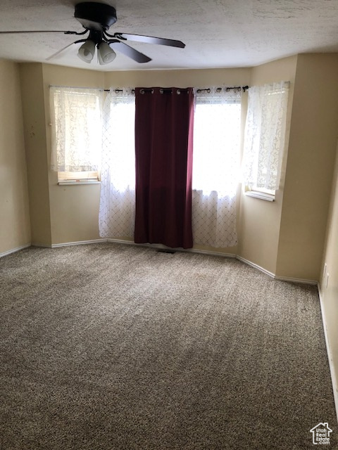 Empty room with a ceiling fan, carpet flooring, baseboards, and a textured ceiling