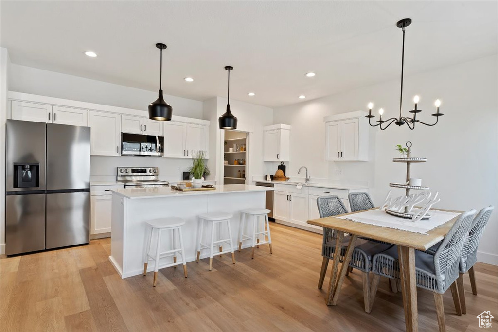 Kitchen with stainless steel appliances, light wood-style floors, light countertops, white cabinets, and a center island