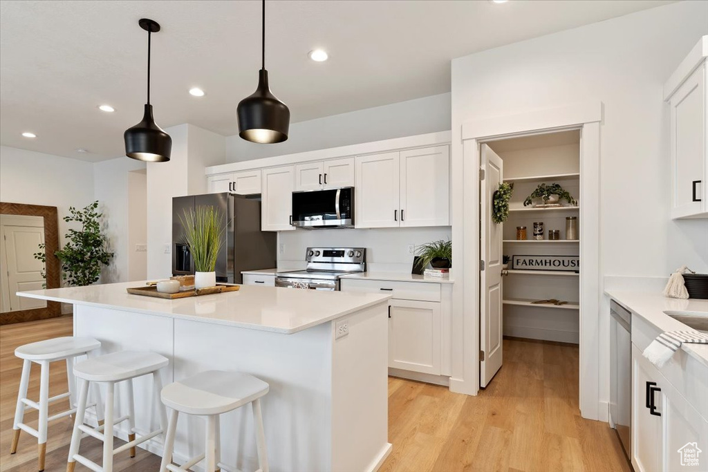 Kitchen featuring appliances with stainless steel finishes, light wood-type flooring, a kitchen breakfast bar, white cabinets, and recessed lighting