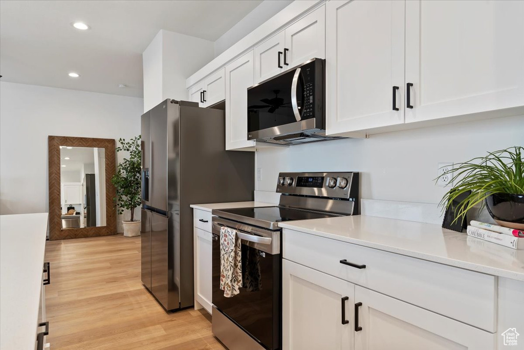 Kitchen featuring stainless steel appliances, light countertops, white cabinetry, light wood-type flooring, and recessed lighting