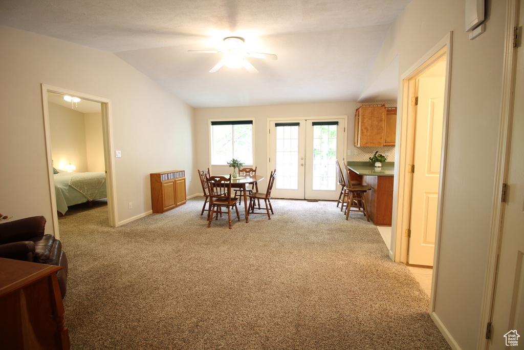 Dining space with vaulted ceiling, a ceiling fan, light carpet, and baseboards