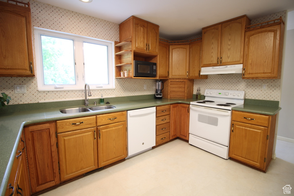 Kitchen featuring white appliances, under cabinet range hood, a sink, tasteful backsplash, and light flooring