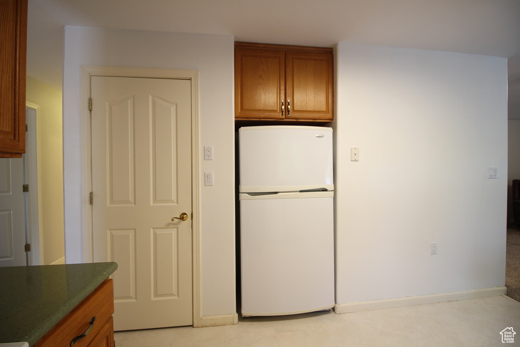 Kitchen with freestanding refrigerator, brown cabinetry, and baseboards