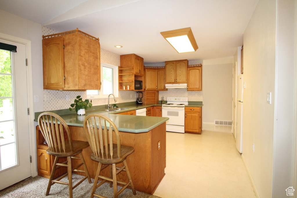 Kitchen with white appliances, under cabinet range hood, a sink, a peninsula, and open shelves