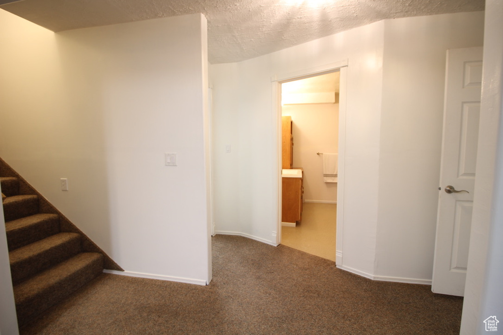 Hallway with a textured ceiling, carpet, stairway, and baseboards