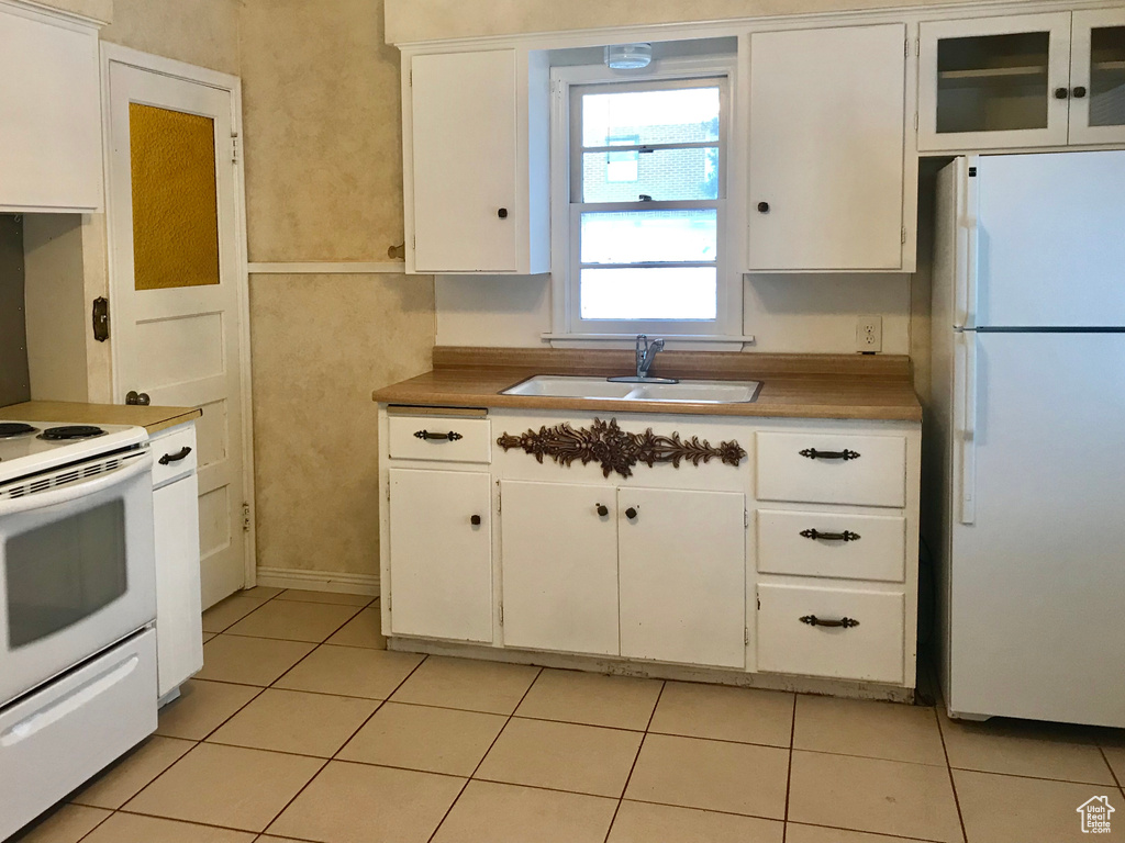 Kitchen featuring white appliances, a sink, white cabinetry, light tile patterned floors, and light countertops