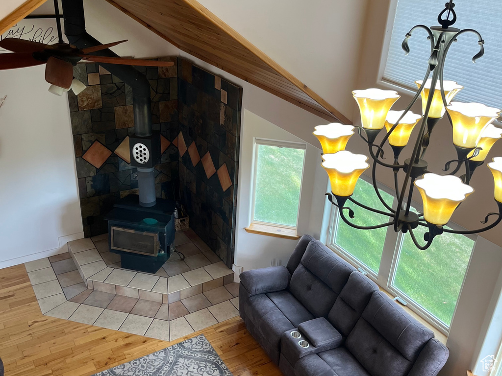 Living room featuring a wood stove, light wood finished floors, lofted ceiling, a ceiling fan, and a chandelier