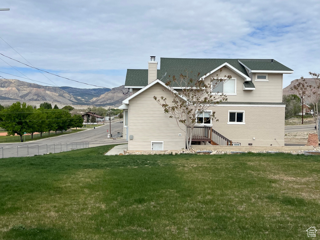 Rear view of house featuring a chimney, a yard, and a mountain view