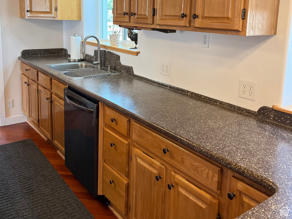 Kitchen with dishwasher, a sink, dark countertops, dark wood-style floors, and brown cabinets