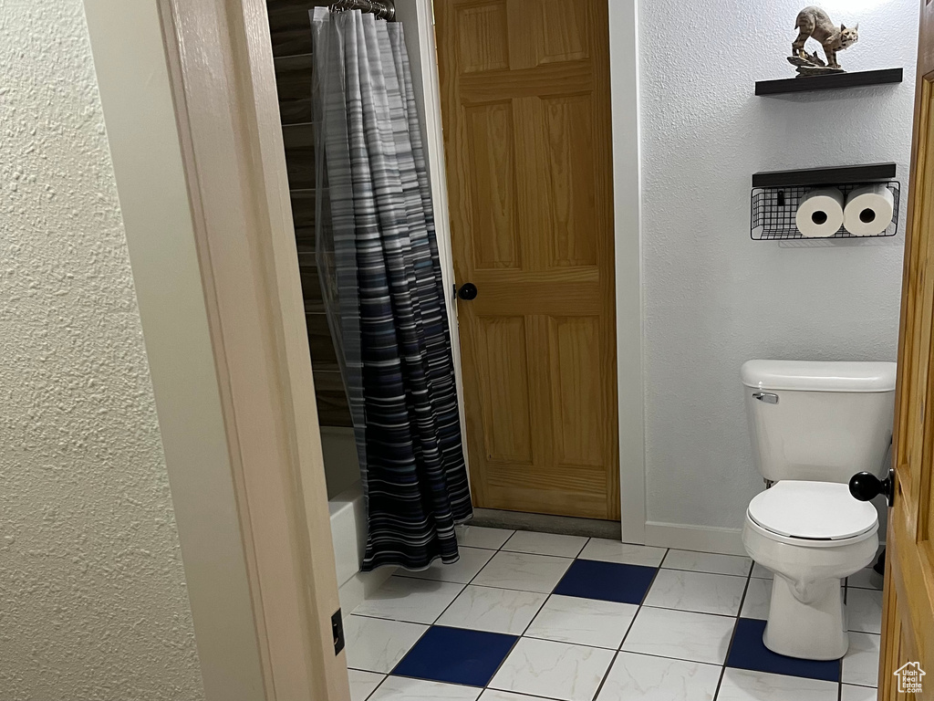 Bathroom with marble finish flooring, toilet, a textured wall, baseboards, and shower / bathtub combination with curtain