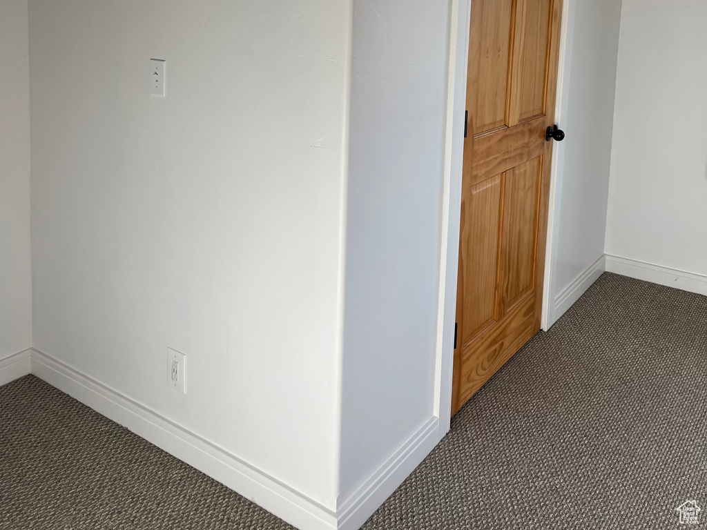 Hall featuring dark colored carpet and baseboards