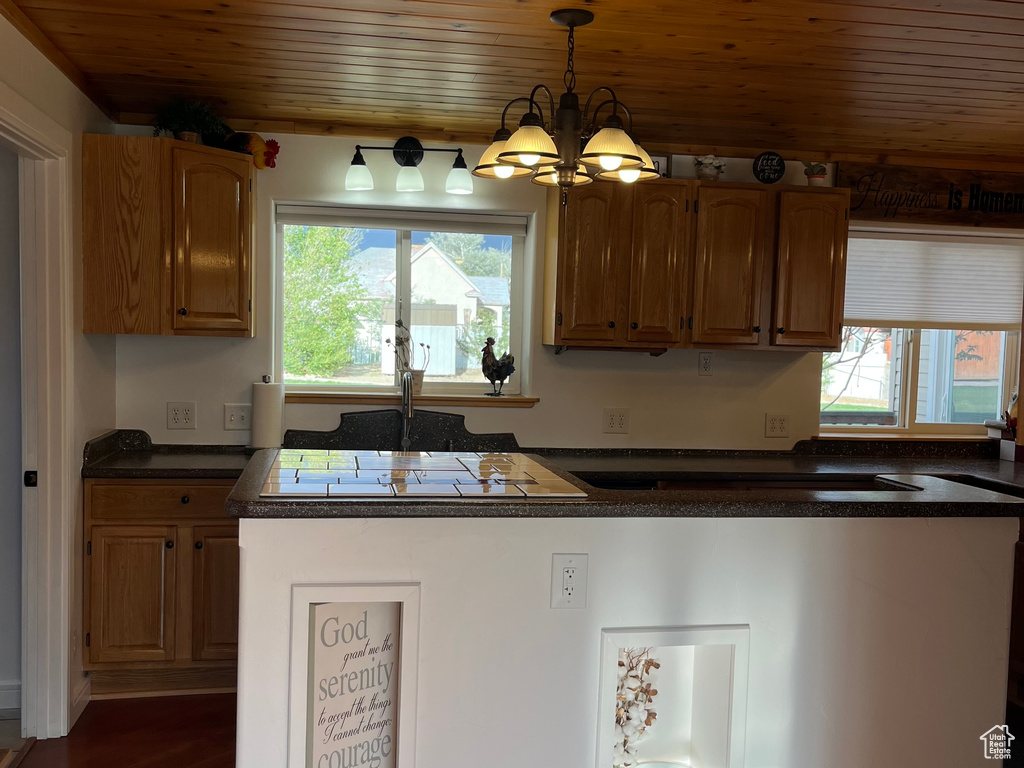 Kitchen with healthy amount of natural light, a chandelier, wooden ceiling, dark countertops, and pendant lighting