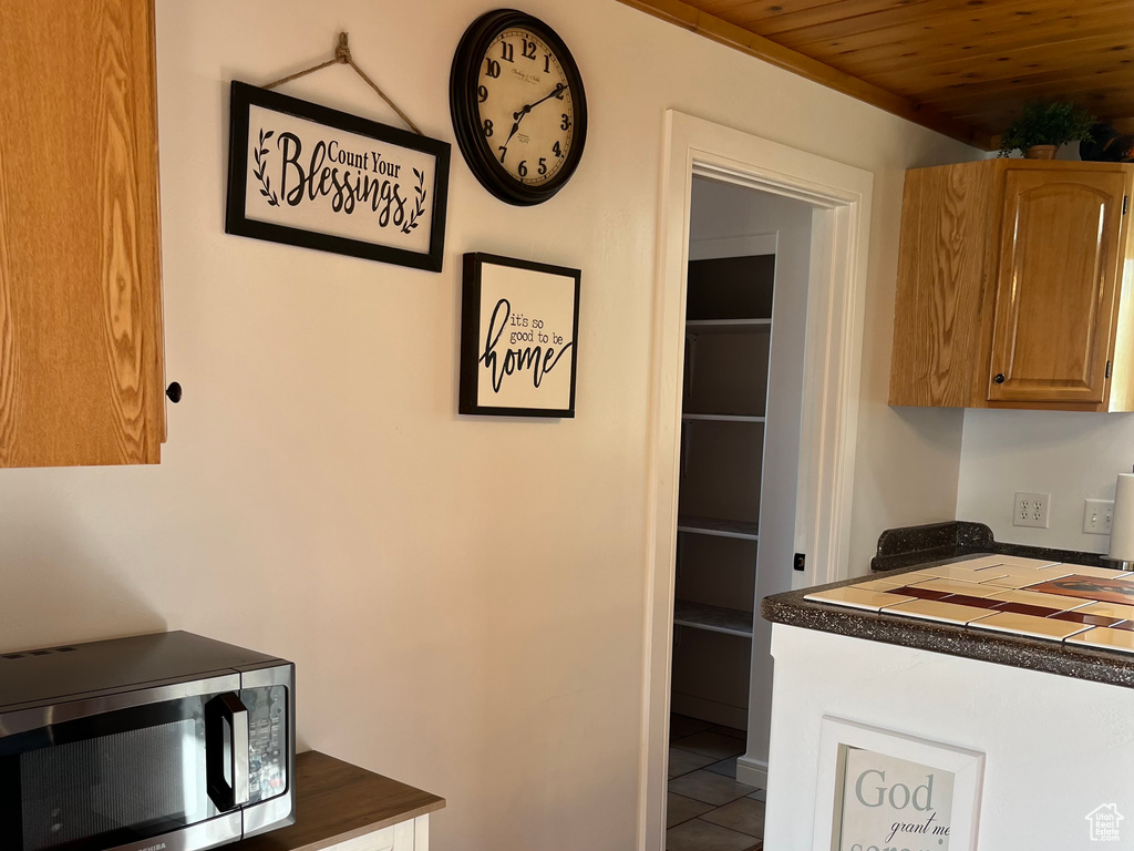 Kitchen featuring stainless steel microwave, dark countertops, tile patterned floors, wood ceiling, and brown cabinets
