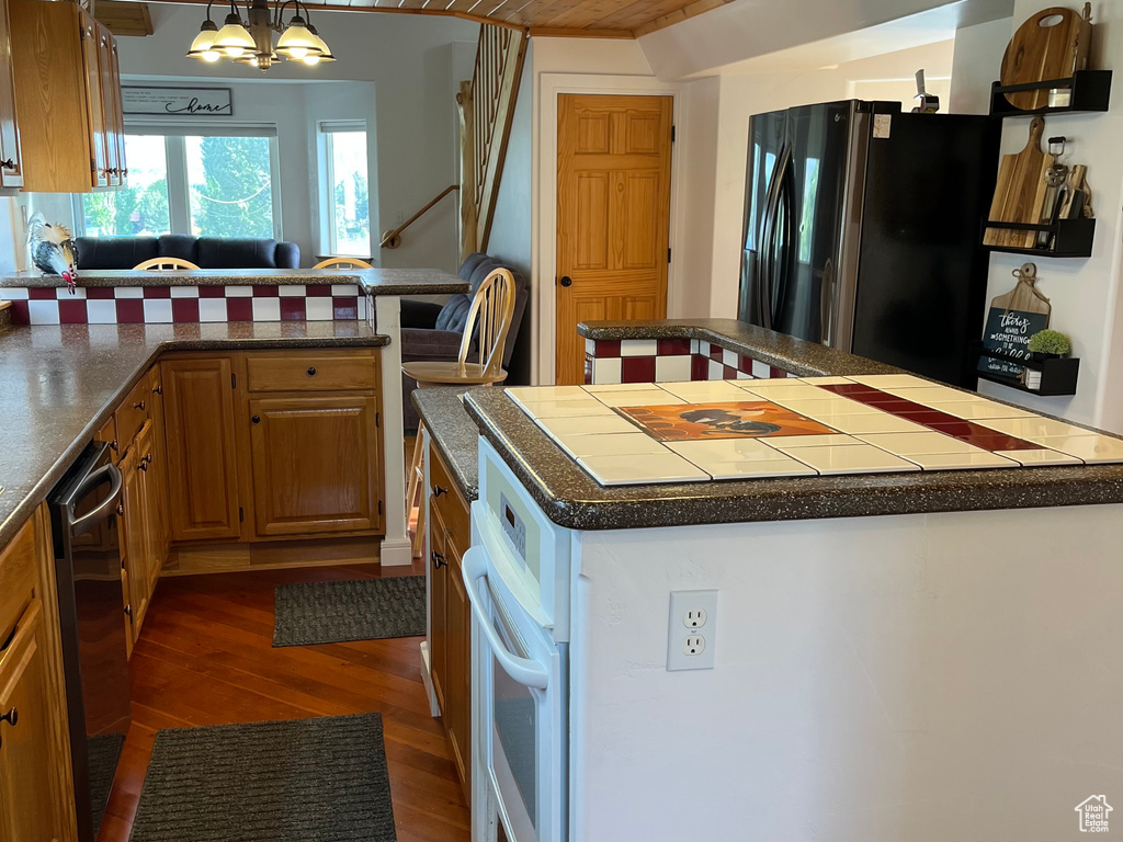 Kitchen featuring freestanding refrigerator, dark wood-style flooring, oven, dishwashing machine, and a kitchen island