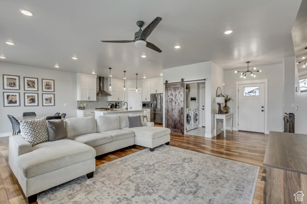 Living room with a barn door, washing machine and clothes dryer, ceiling fan, baseboards, and wood finished floors