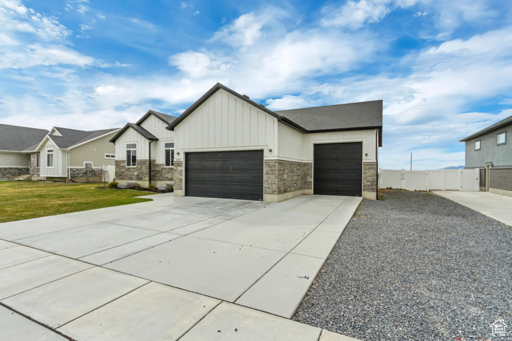 View of front facade with board and batten siding, an attached garage, concrete driveway, and stone siding