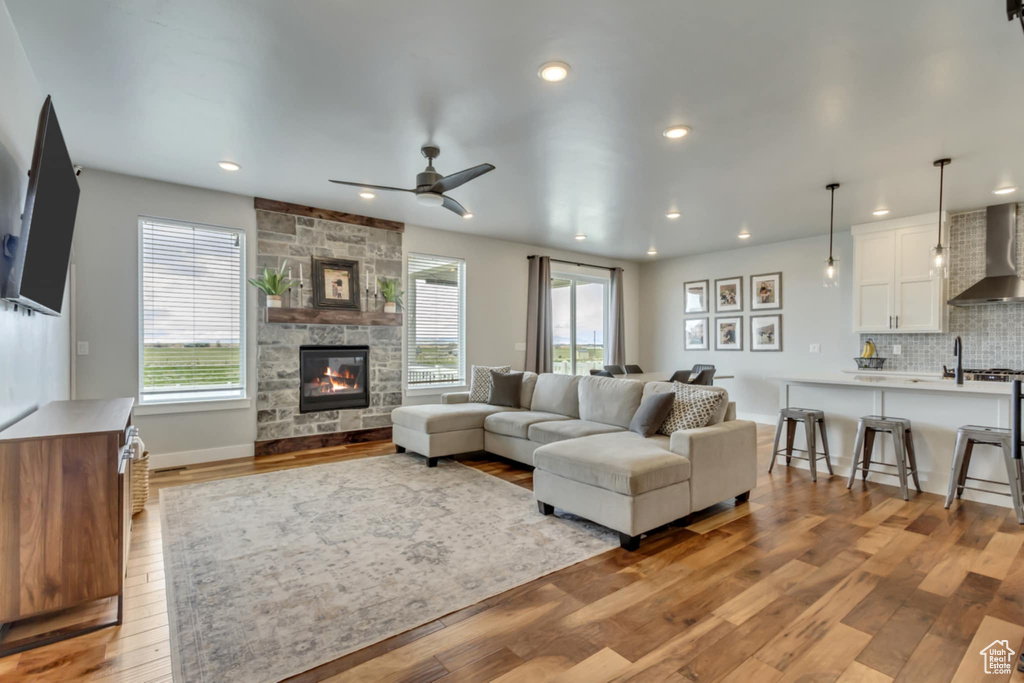 Living area with hardwood / wood-style flooring, a stone fireplace, a ceiling fan, recessed lighting, and baseboards