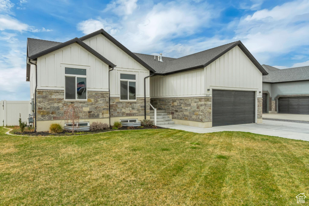 View of front of home with board and batten siding, a garage, driveway, stone siding, and roof with shingles