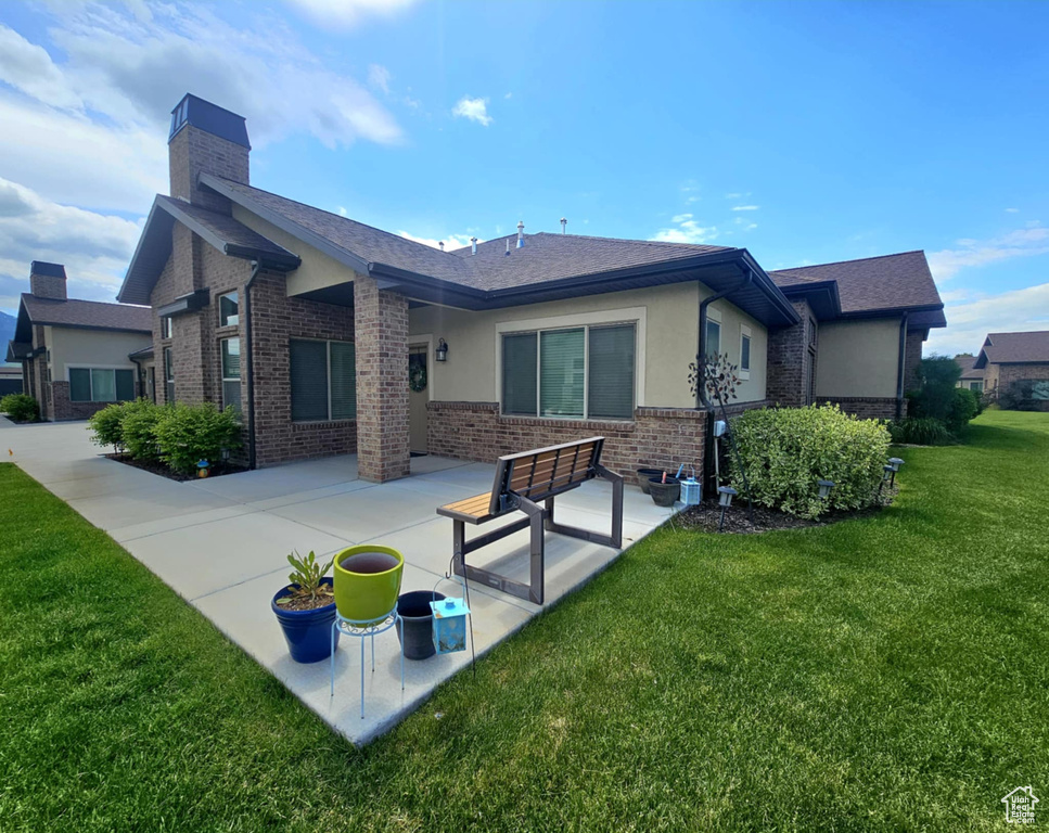 Back of house featuring brick siding, a yard, a chimney, a patio, and stucco siding