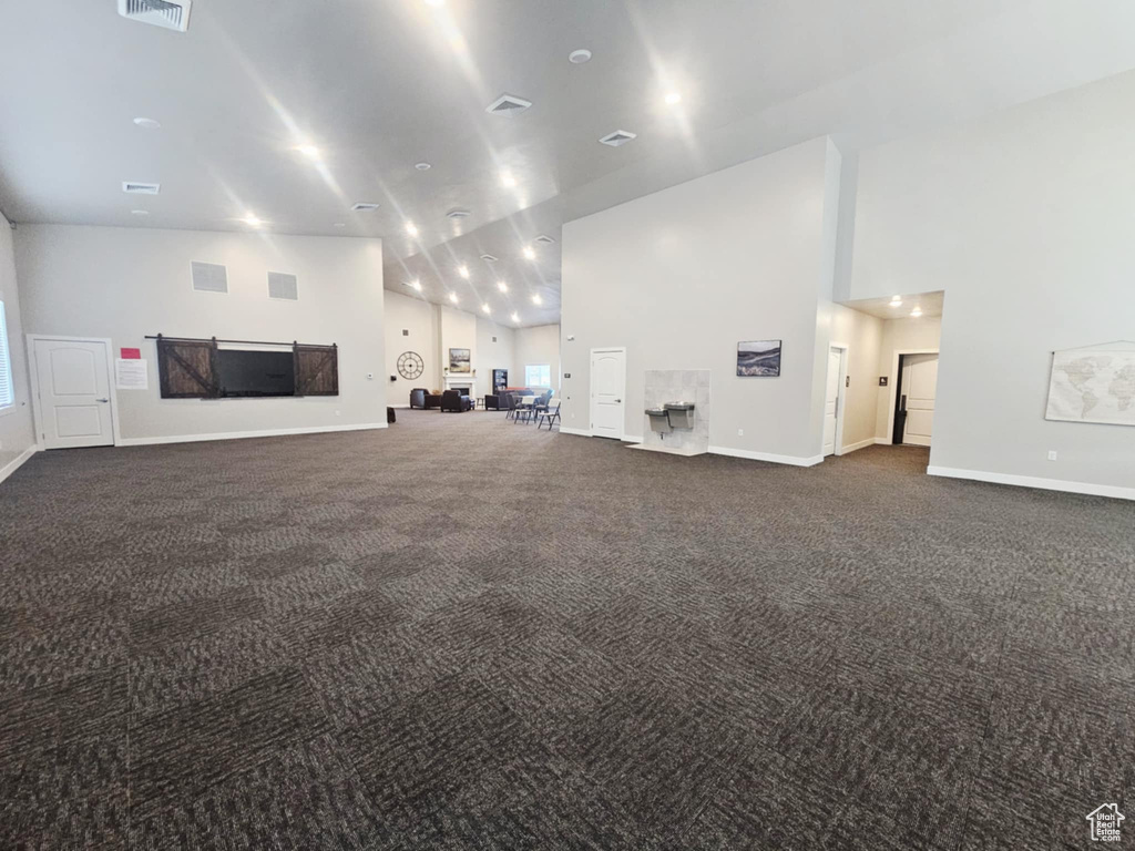 Unfurnished living room featuring high vaulted ceiling, dark carpet, and baseboards