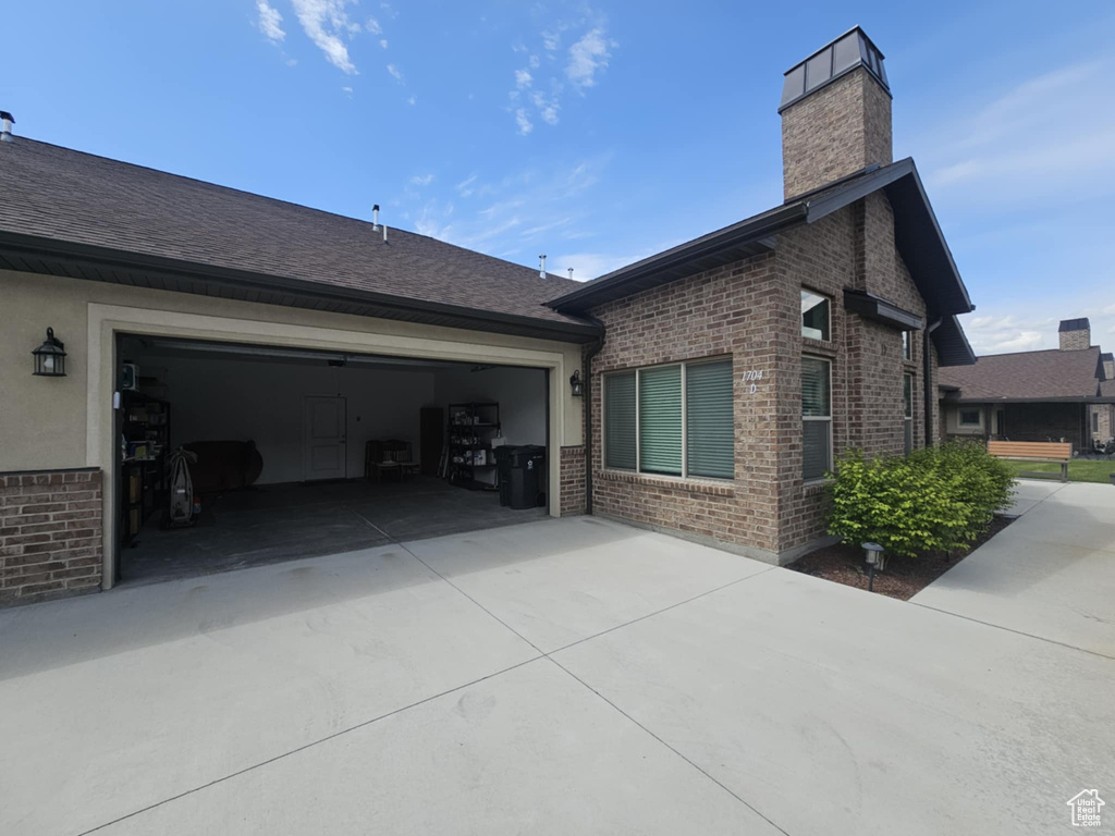 View of side of property featuring brick siding, a chimney, concrete driveway, and a shingled roof