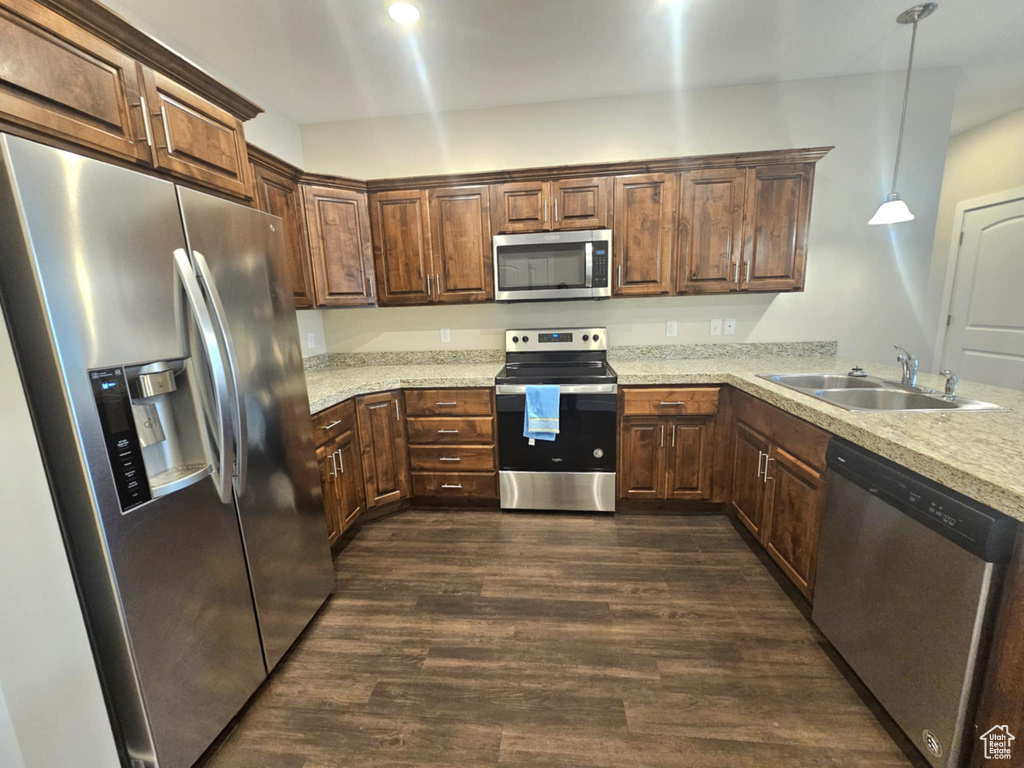 Kitchen with appliances with stainless steel finishes, a sink, dark wood finished floors, pendant lighting, and a peninsula
