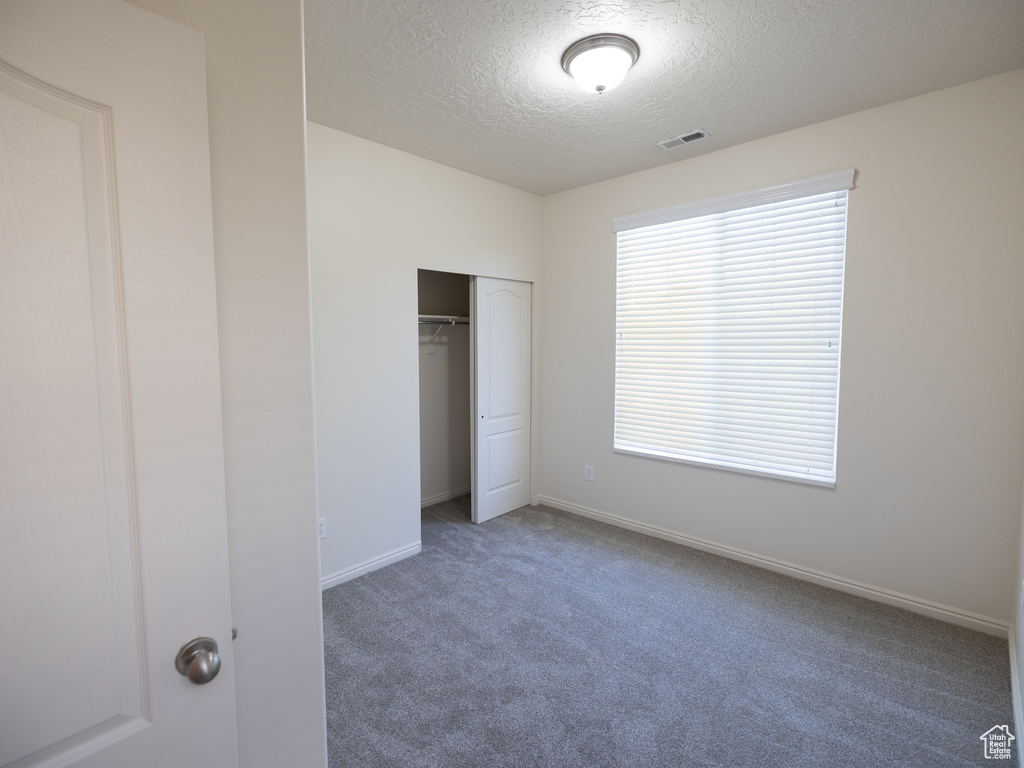 Unfurnished bedroom with a textured ceiling, carpet floors, a closet, and baseboards