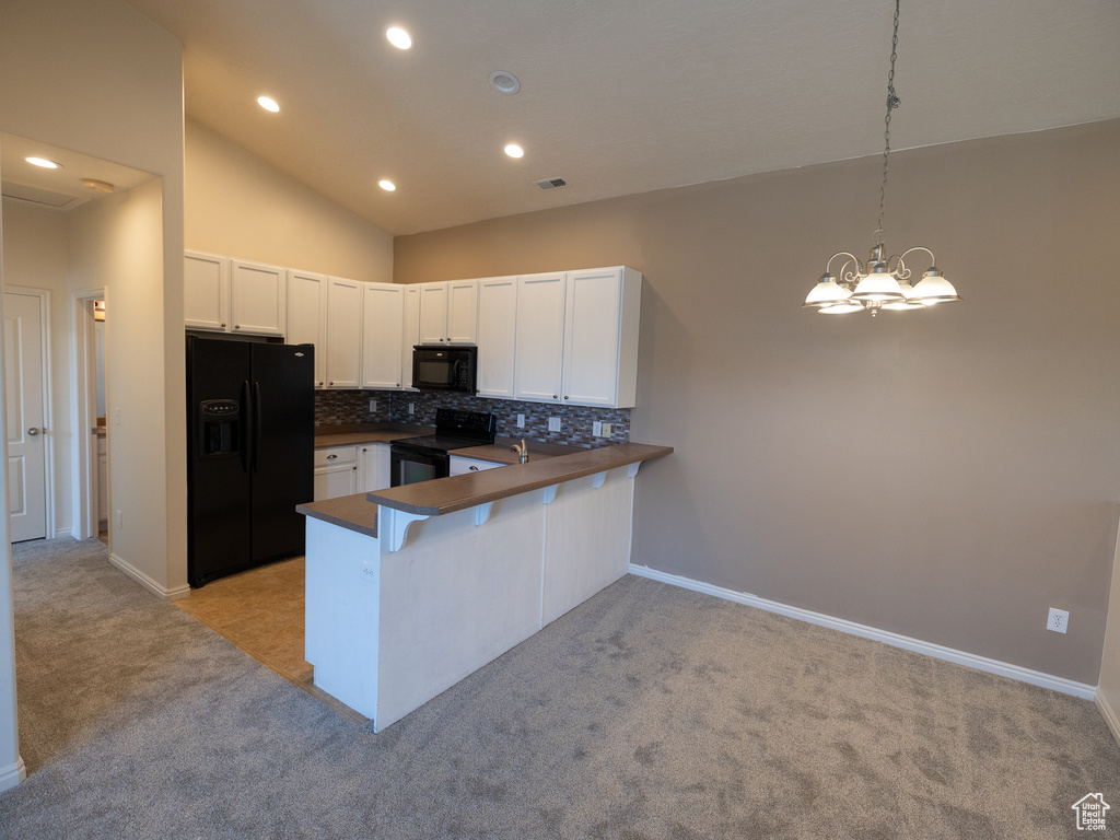 Kitchen with black appliances, dark countertops, light carpet, a peninsula, and decorative backsplash