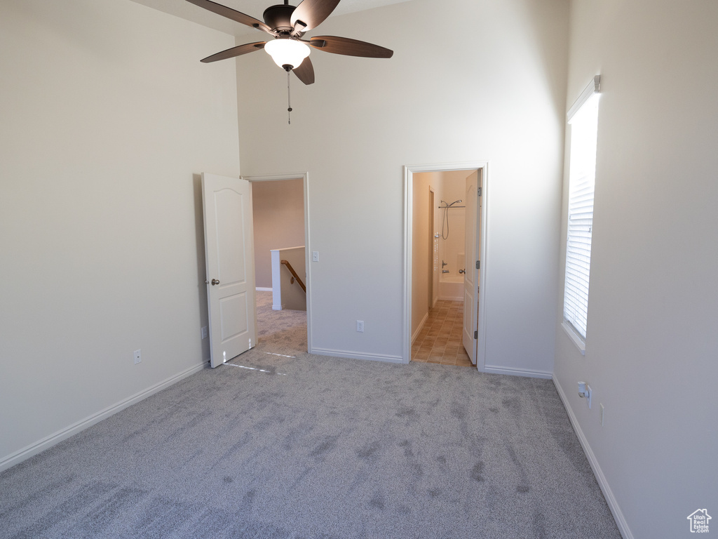 Unfurnished bedroom featuring a high ceiling, light carpet, baseboards, multiple windows, and ensuite bathroom
