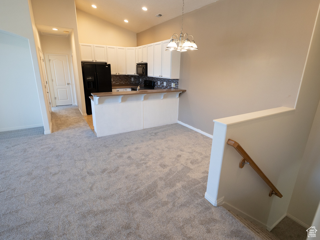 Kitchen featuring black appliances, backsplash, white cabinets, a chandelier, and light colored carpet