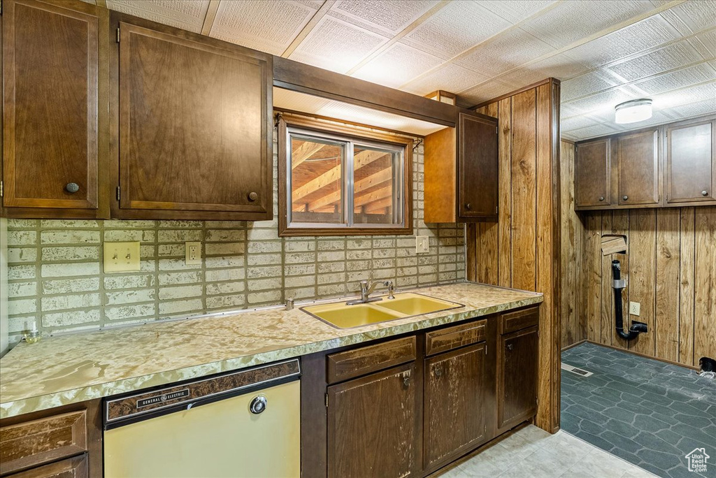 Kitchen with dishwasher, a sink, light countertops, wood walls, and decorative backsplash
