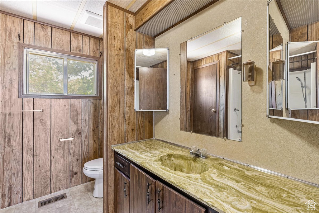 Bathroom featuring toilet, vanity, wooden walls, and a textured wall
