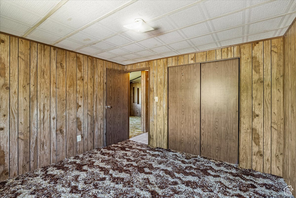 Unfurnished bedroom with wooden walls, carpet flooring, and a closet