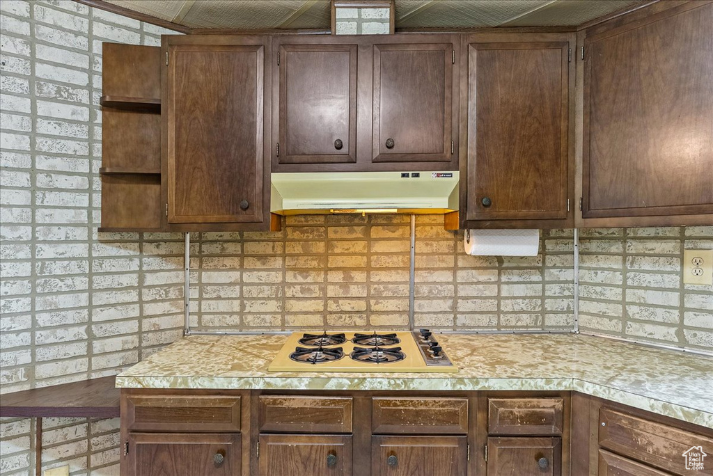 Kitchen with under cabinet range hood, white cooktop, light countertops, and decorative backsplash