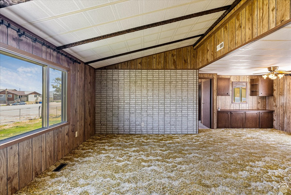 Unfurnished living room featuring wooden walls, vaulted ceiling, carpet floors, and ceiling fan