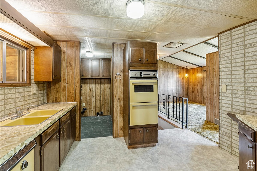 Kitchen with a sink, wooden walls, light countertops, light floors, and white double oven
