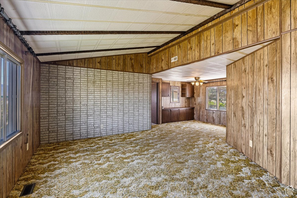 Unfurnished living room featuring carpet floors, wooden walls, vaulted ceiling, and ceiling fan