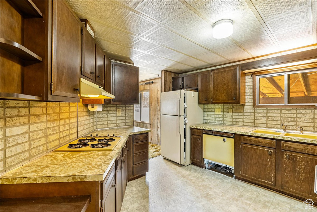 Kitchen featuring white appliances, open shelves, under cabinet range hood, light countertops, and a sink
