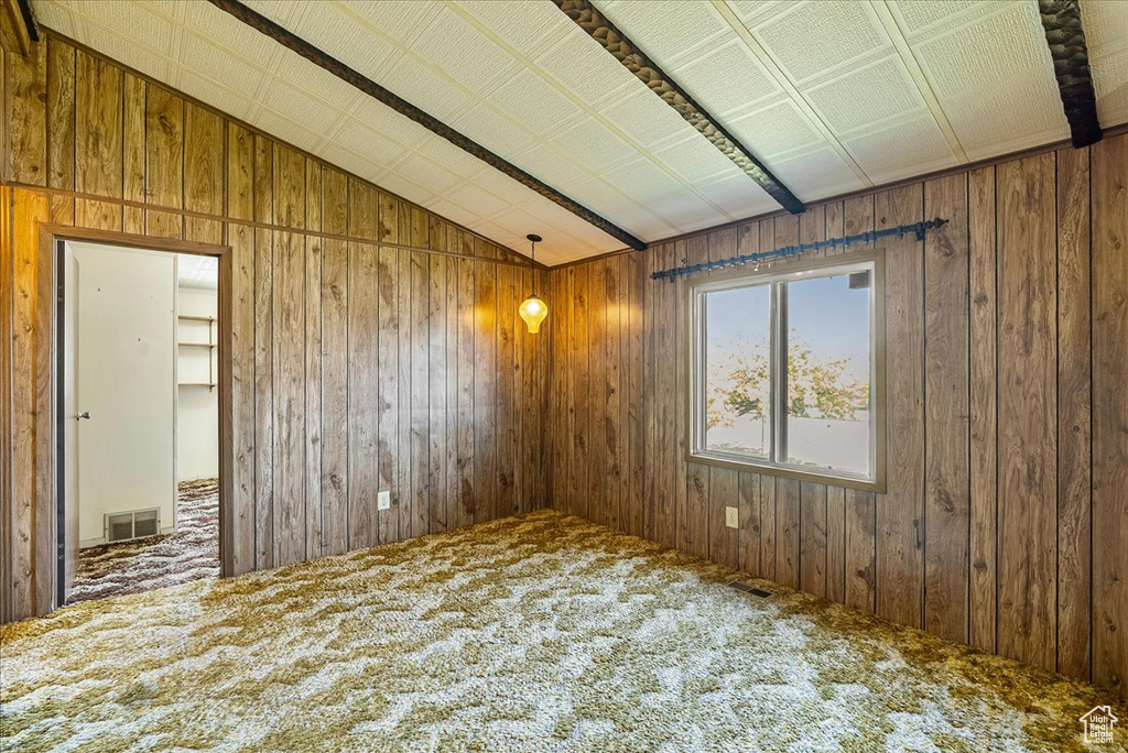 Carpeted empty room with vaulted ceiling and wood walls