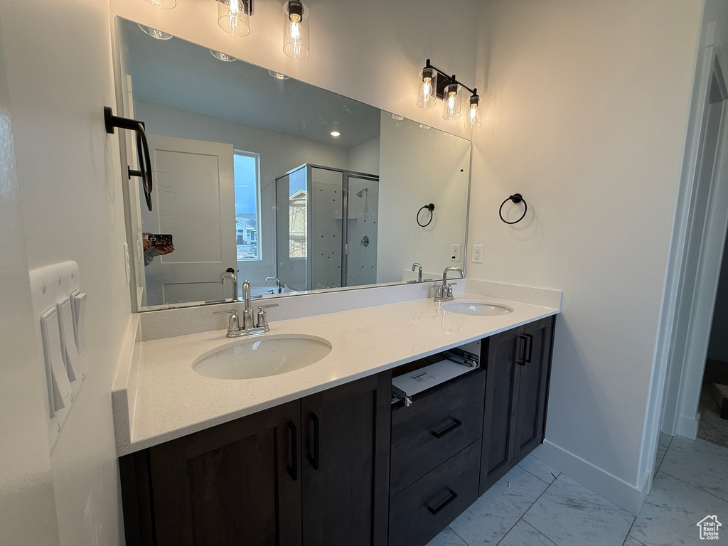 Bathroom featuring a shower stall, double vanity, marble finish flooring, and baseboards