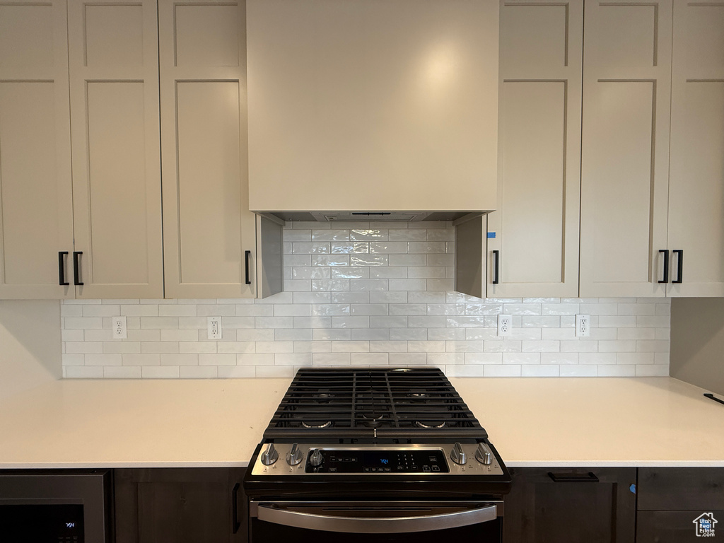 Kitchen with stainless steel gas range oven, light countertops, decorative backsplash, and custom range hood